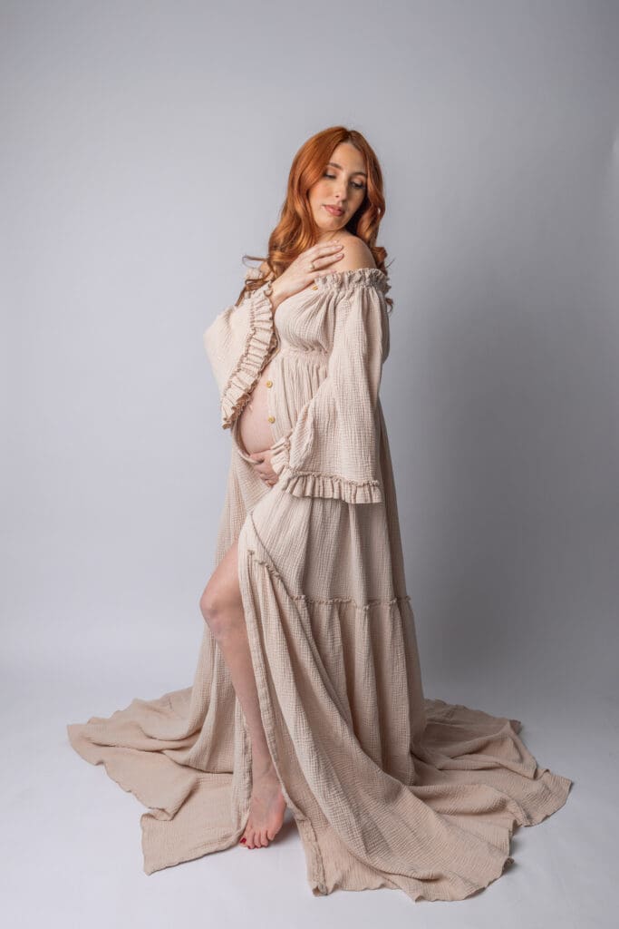 Photo of an expecting mom in a beautiful beige gown gently holding her belly