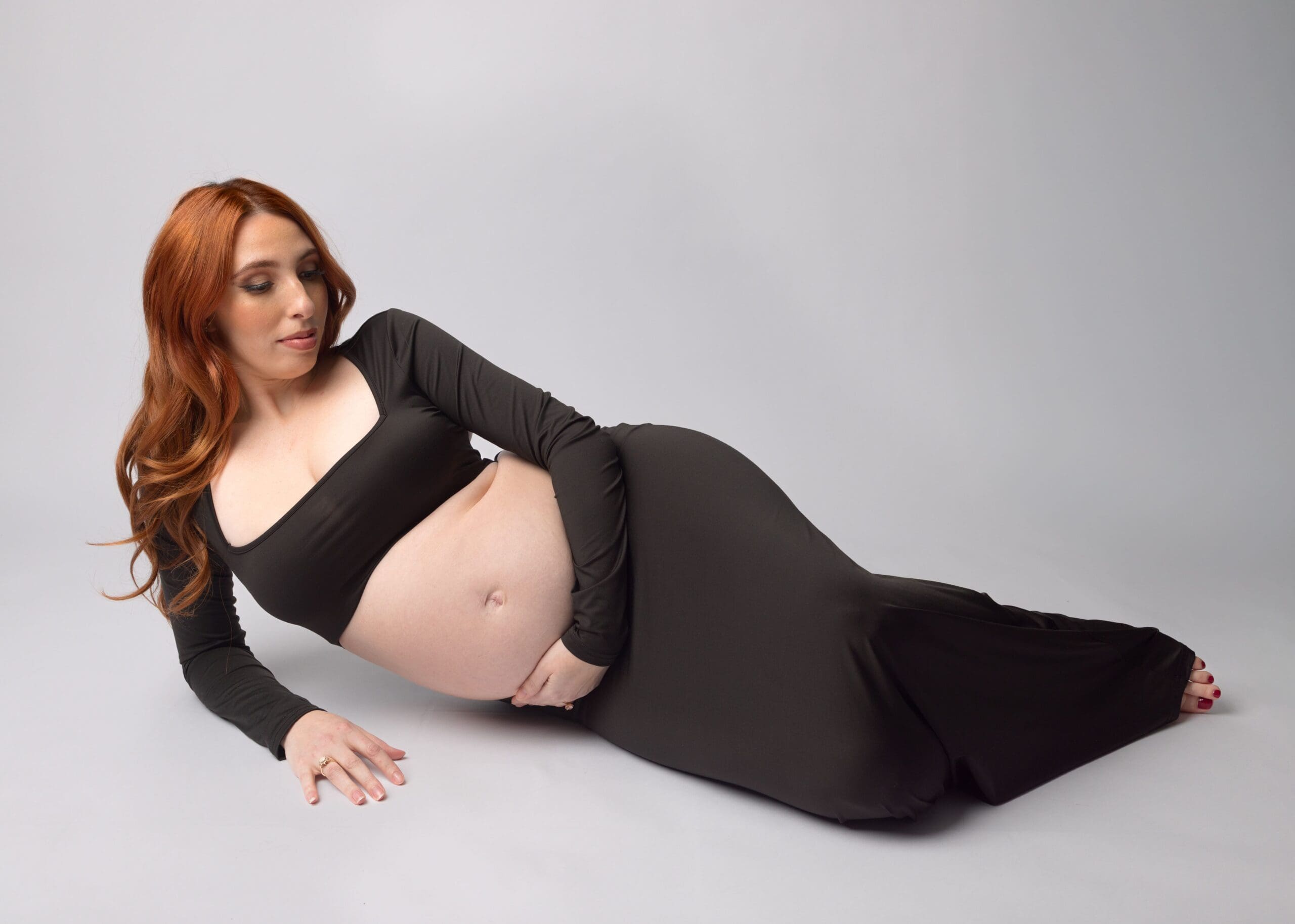 Expecting mom in a black track laying on the floor on her side gently holding her belly