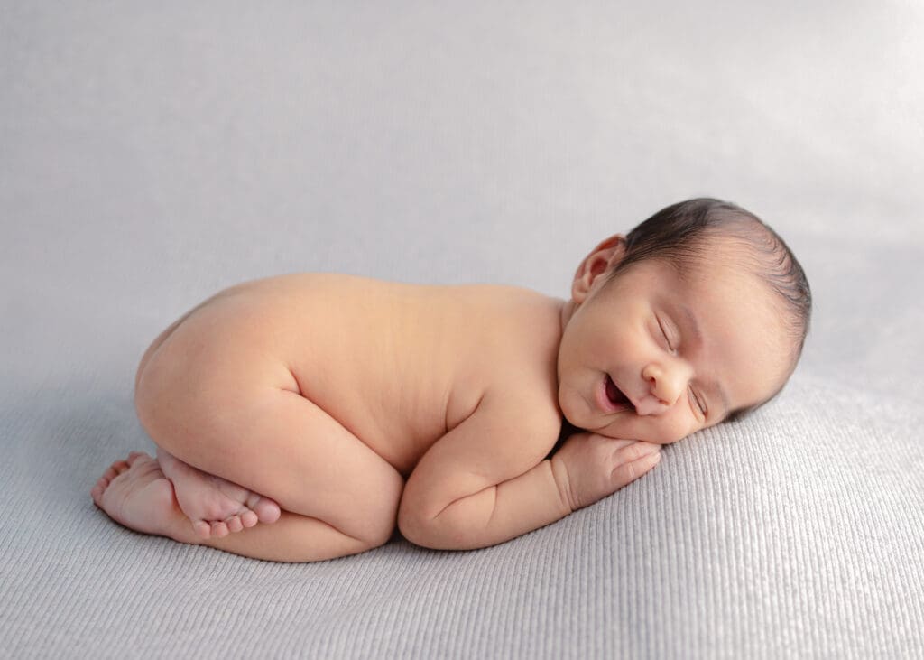 Photo of a naked newborn in tushy pose with a cute smile on his face