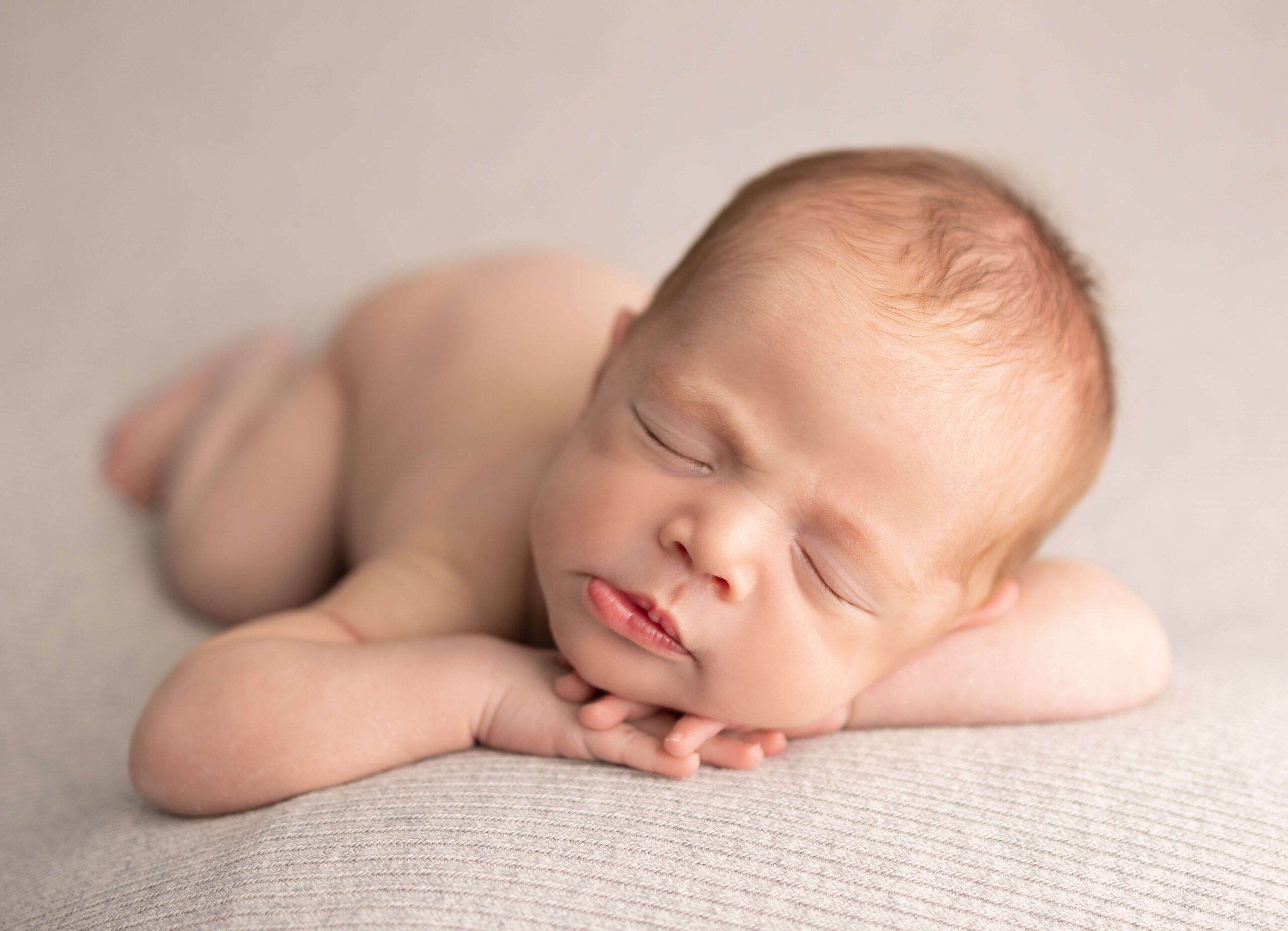 A naked sleeping newborn baby on its hands in a studio