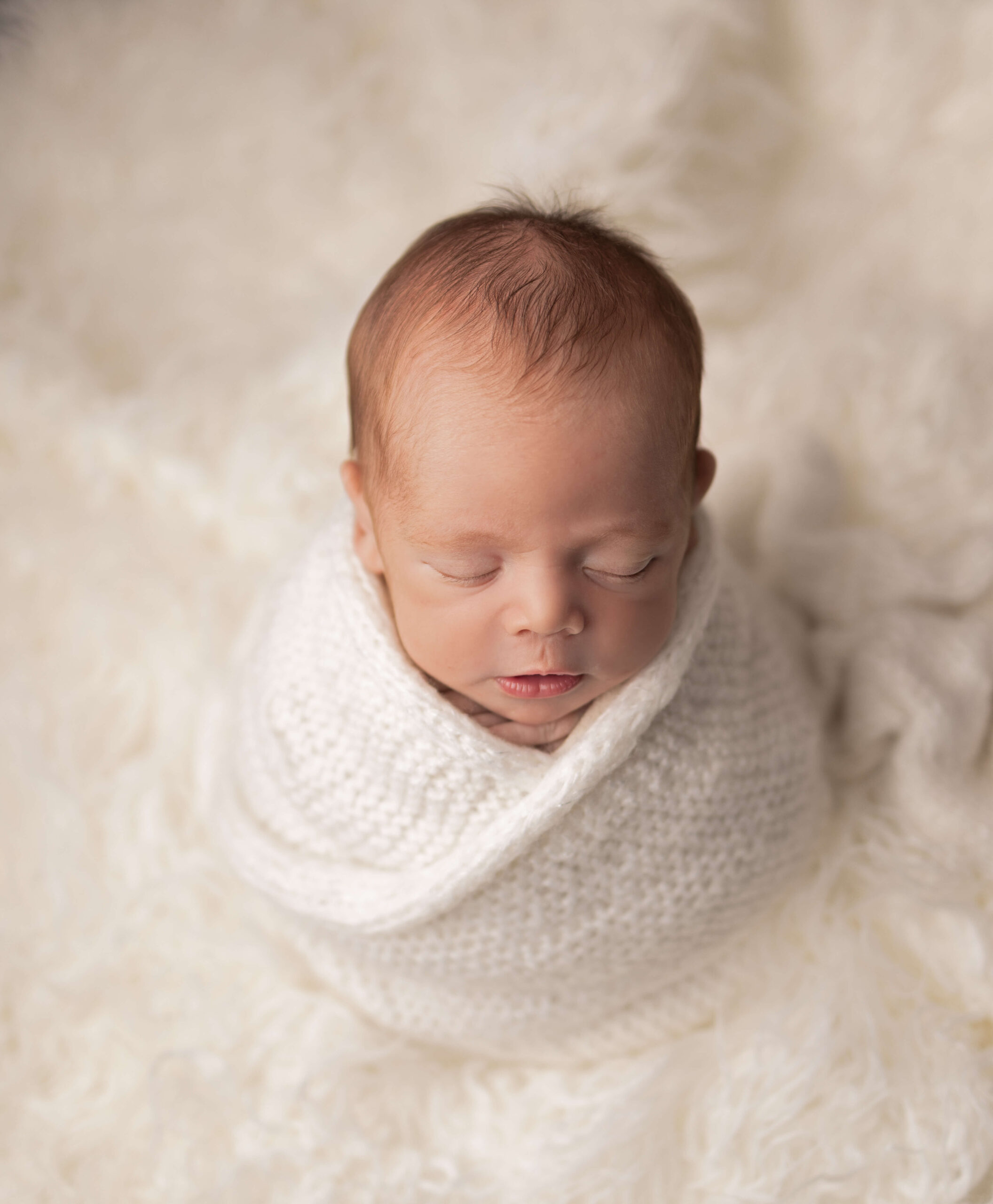 A sleeping newborn baby in a white knit swaddle on a fur blanket thanks to lactation consultants in bergen county nj