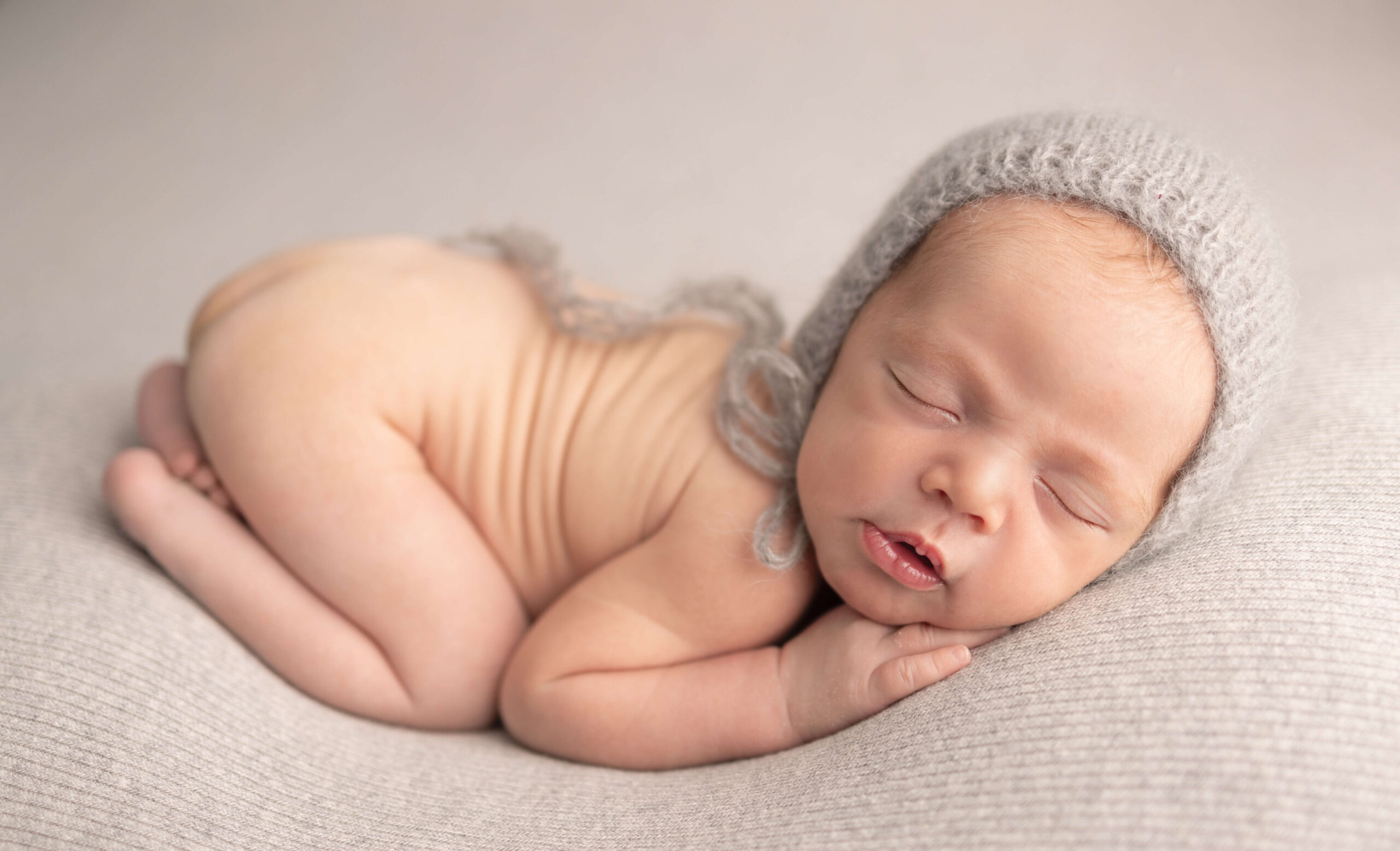 A newborn baby sleeps in froggy pose wearing only a grey knit bonnet after meeting lactation consultants in bergen county nj