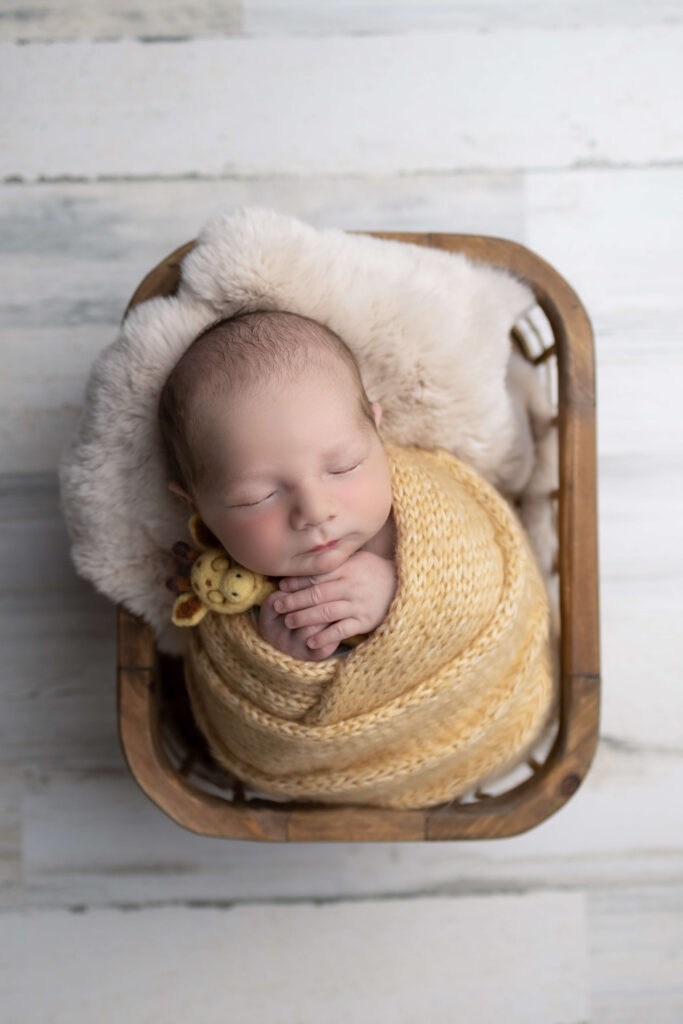A sleeping newborn in a yellow knit swaddle in a wooden crate after meeting a nanny in bergen county nj