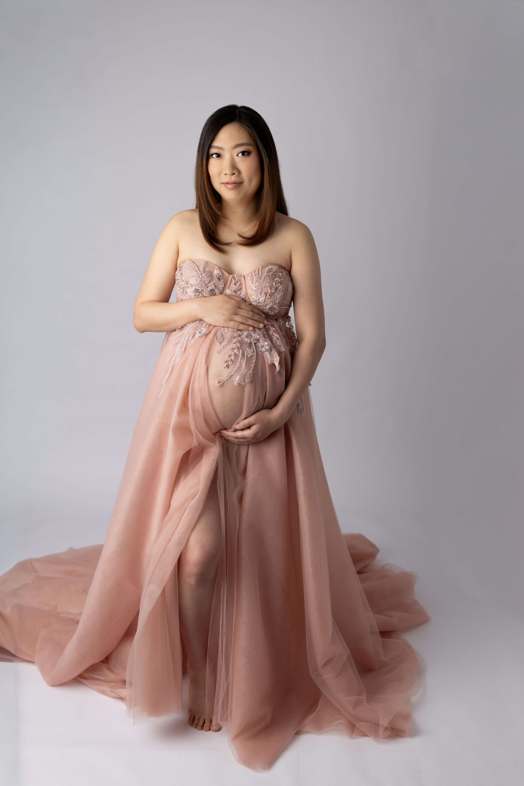 A mom to be stands in a studio in a pink maternity gown in a studio after visiting our birthing center morristown