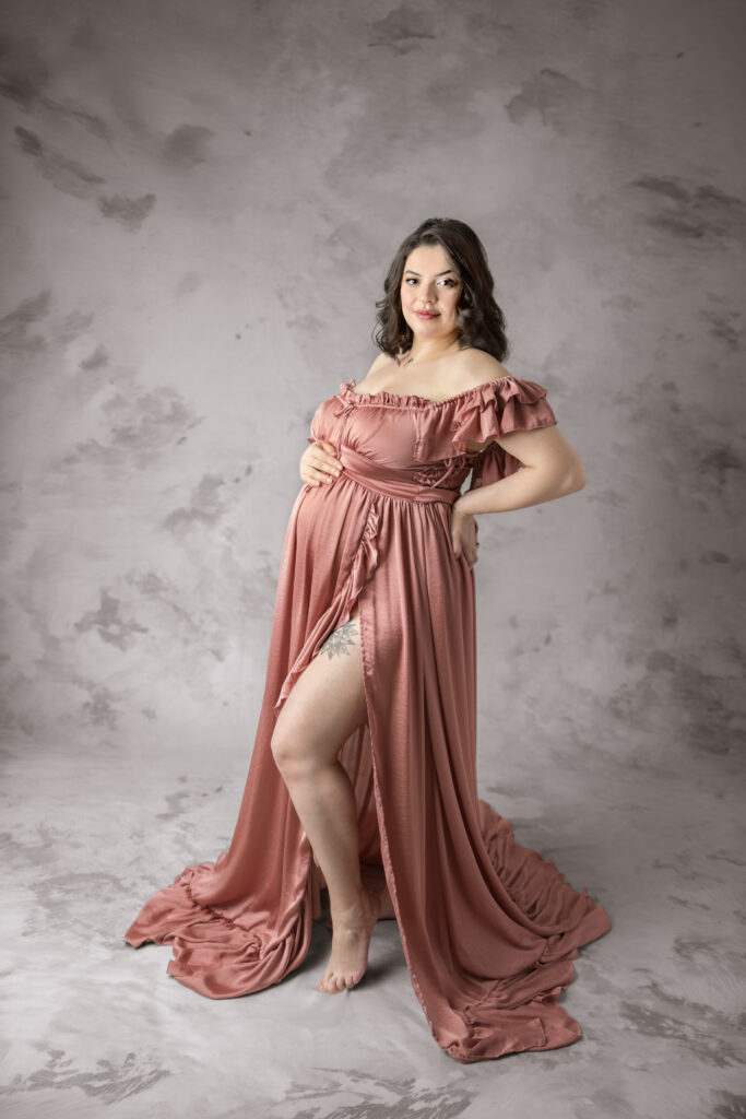 Confident maternity portrait in a rose gown with ruffled sleeves and soft lighting in Clifton, NJ.