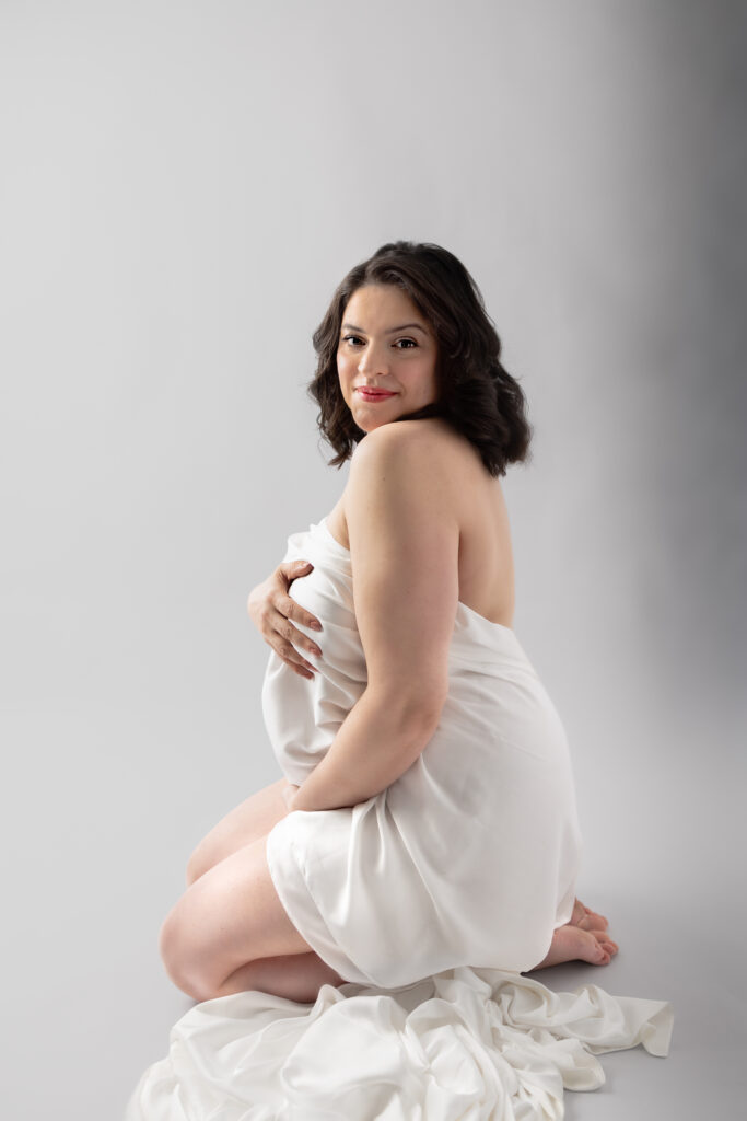Clifton, NJ maternity photography featuring an expectant mother wrapped in white fabric, gazing toward her baby bump.