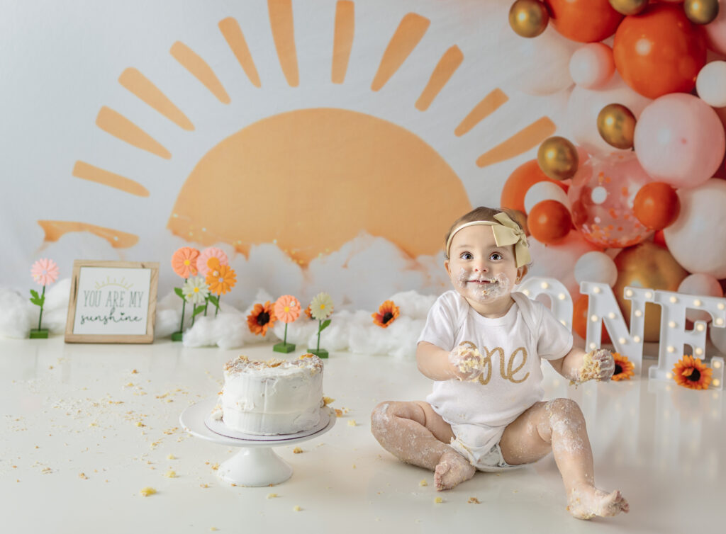 Sweet one-year-old girl smiles from a milk bath during her birthday photo session.