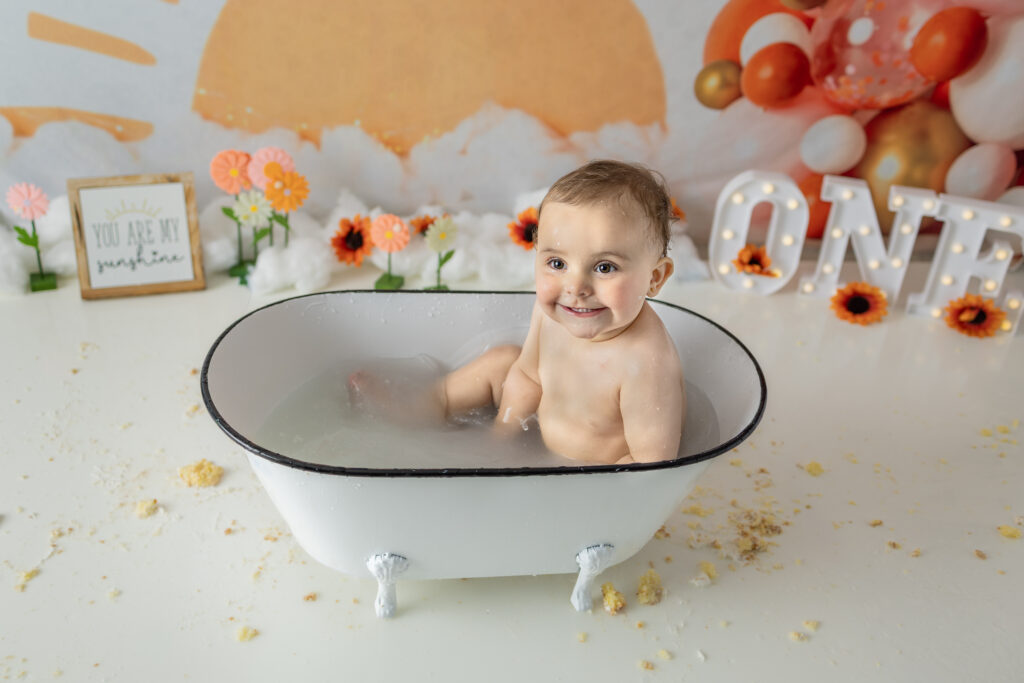 Happy birthday girl laughs in a vintage bathtub after her cake smash celebration.