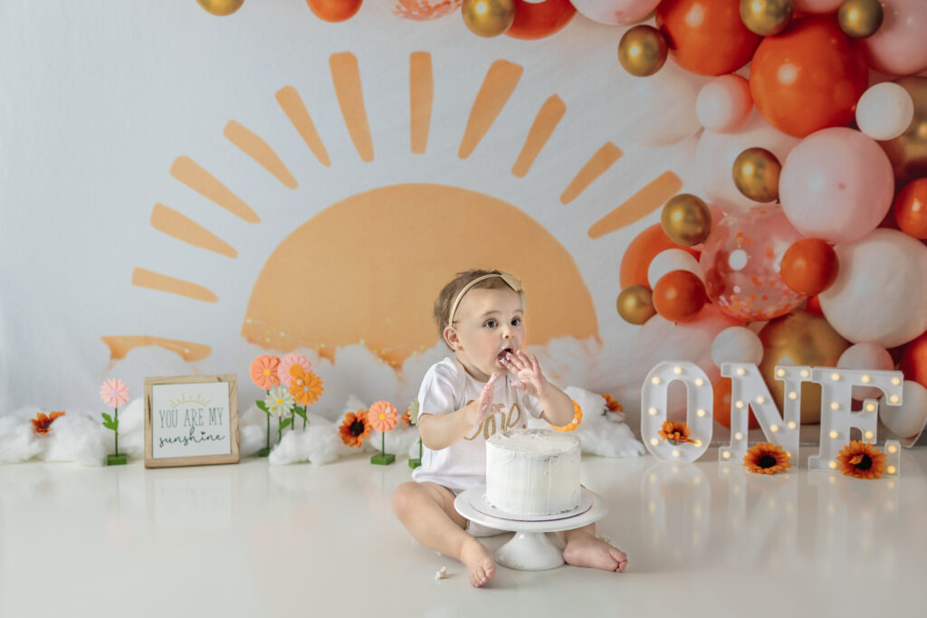 Baby girl tastes frosting from her birthday cake during a first birthday cake smash session.