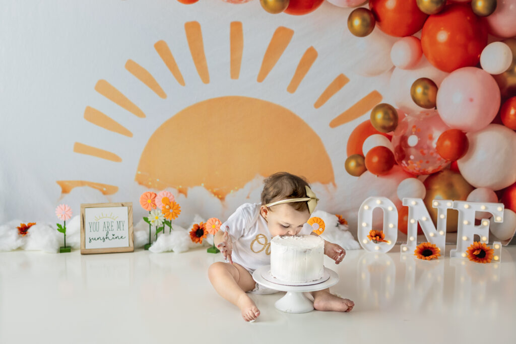 One-year-old girl enjoys birthday cake beneath a sunshine backdrop during her cake smash session.