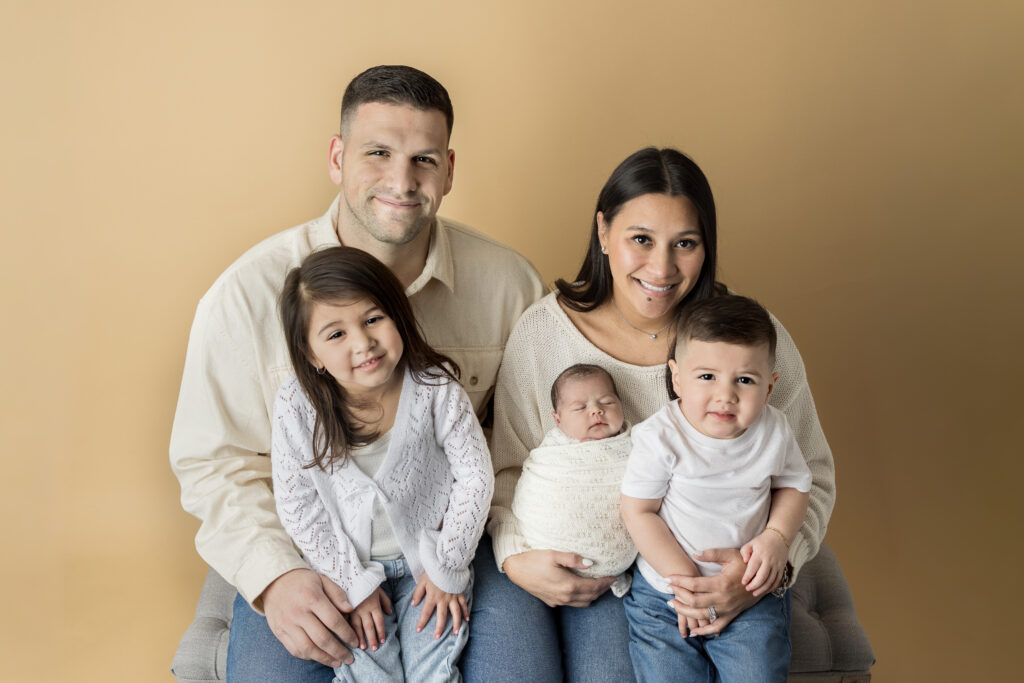 Family of five poses together with their swaddled newborn baby in Jersey City, NJ studio.