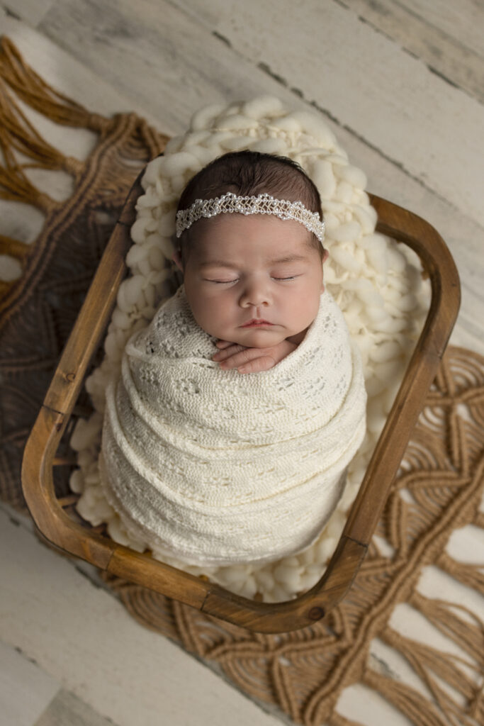 Sleeping newborn rests in a wooden crate with cream wrap and pearl headband in Jersey City