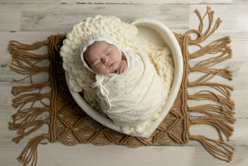 Swaddled baby sleeps in a heart-shaped bowl on a textured rug in Jersey City, NJ.