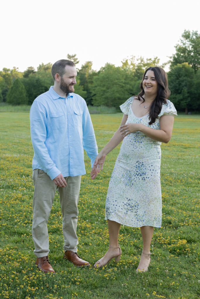 Couple laughs together while holding hands in a grassy field filled with tiny yellow flowers.
