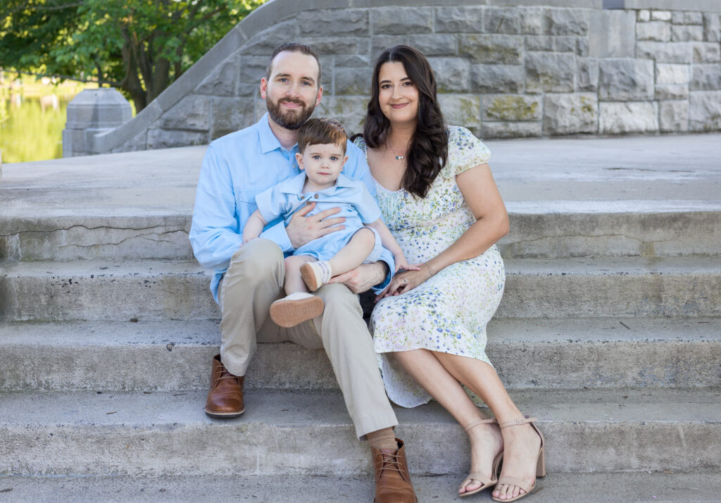 Family of three sits closely on stone steps during a summer portrait in Bergen County, NJ.