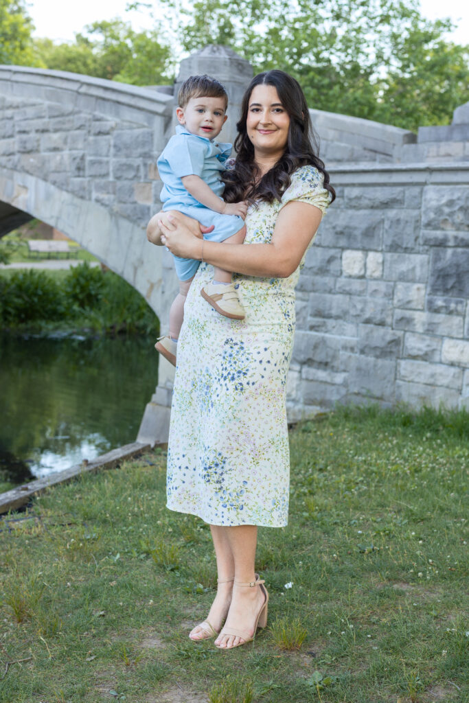 Mother holds toddler beside a stone bridge during an outdoor Bergen County, NJ family session.