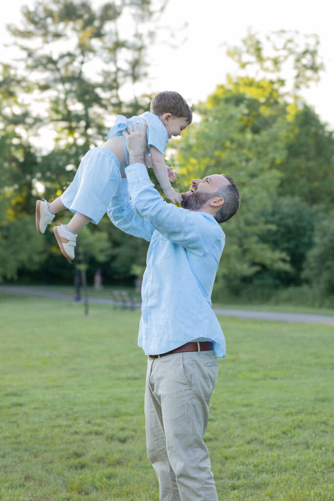 Father lifts toddler high in the air during a playful Bergen County, NJ family portrait.