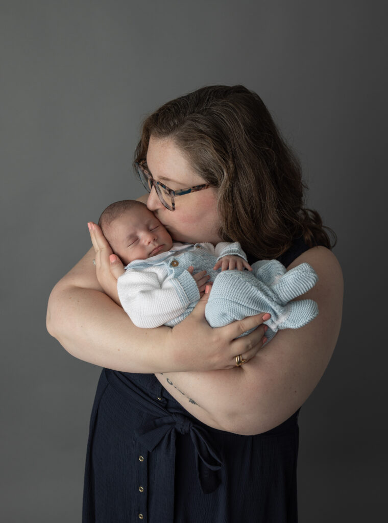 Mother kisses her newborn baby while cuddling him closely, creating a tender and intimate studio newborn portrait.