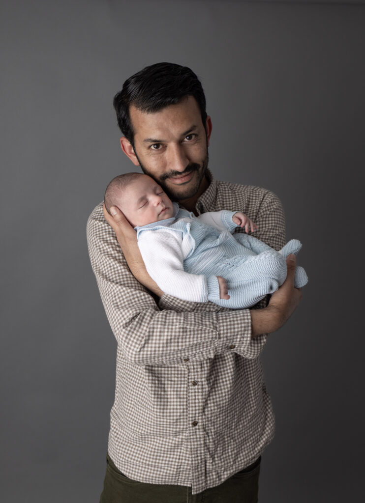 Bergen County, NJ newborn photographer captures father gently holding his sleeping baby in a timeless studio portrait.