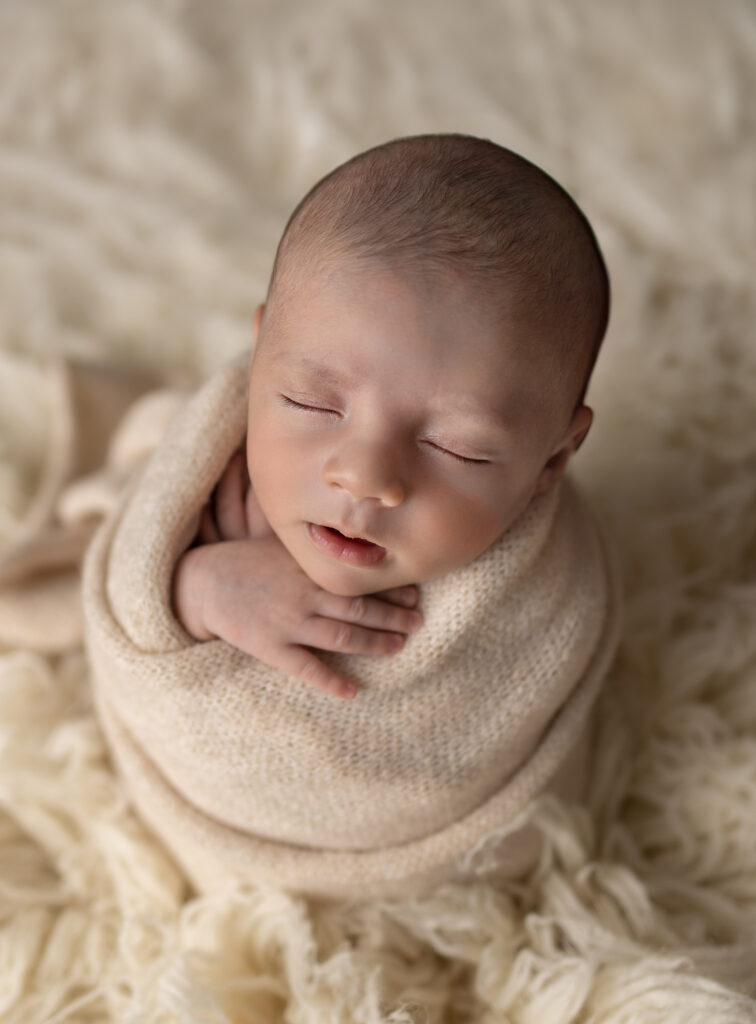 Bergen County, NJ newborn photography session featuring baby swaddled in a cream wrap with tiny hands resting together.