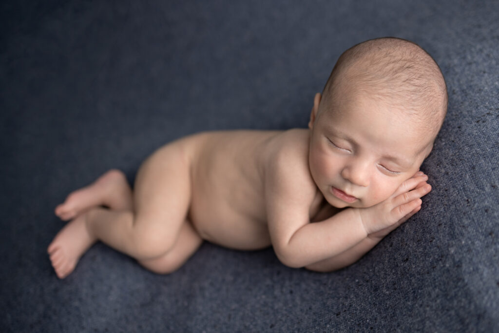 Bergen County, NJ newborn photography captures a sleepy baby naturally posed on a dark blue textured blanket.
