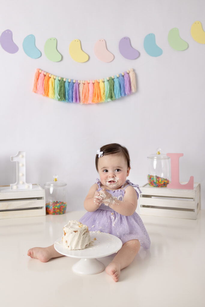 Clifton, NJ cake smash photos feature a smiling baby girl covered in frosting enjoying her first birthday cake.