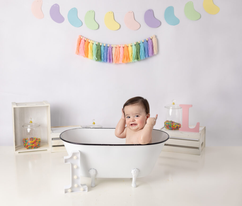 Clifton, NJ cake smash photography captures a baby girl enjoying her birthday cake beneath pastel rainbow decorations.