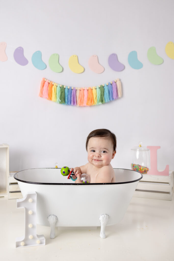 Clifton, NJ first birthday photos feature a smiling baby girl in a white vintage bathtub after cake smash.