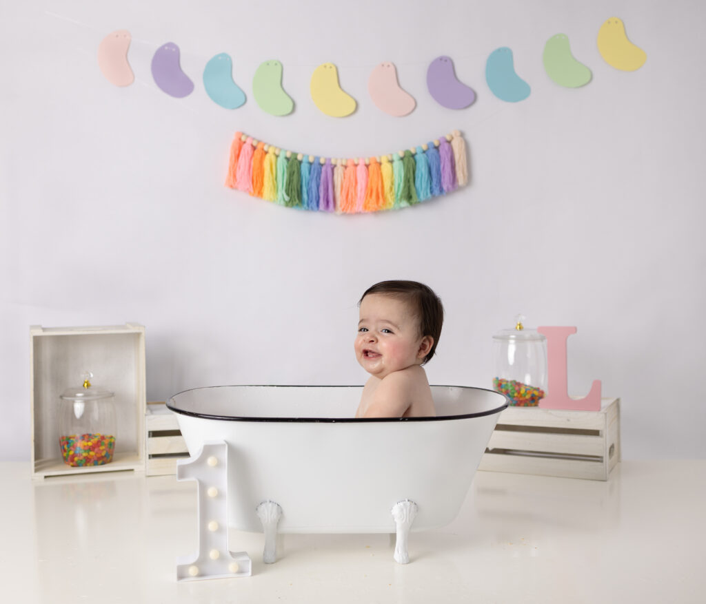 Baby girl smiles in a vintage white bathtub after her first birthday cake smash.