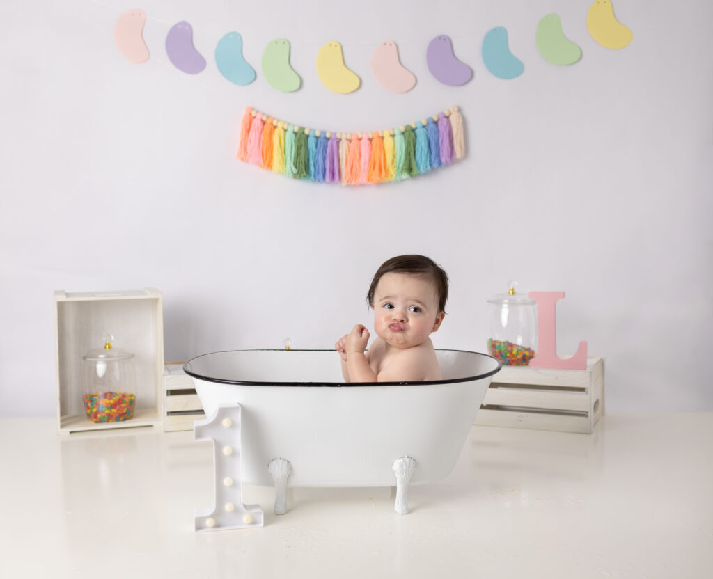 Baby girl makes a silly face in a vintage white bathtub after her first birthday cake smash in Clifton, NJ.