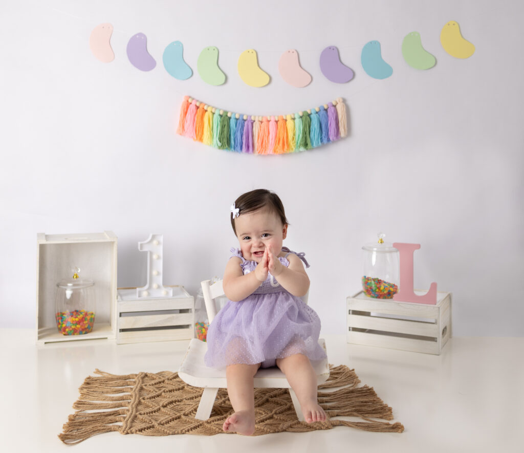 Clifton, NJ cake smash photos capture a baby girl happily claps her hands.