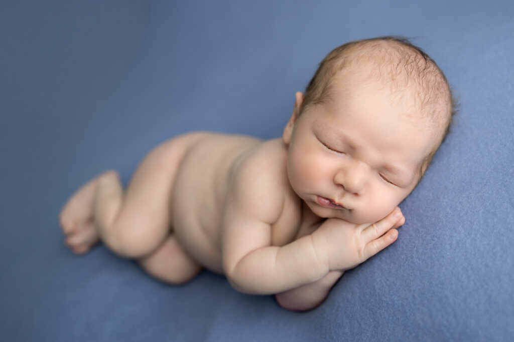 Clifton, NJ newborn photographer captures a sleepy baby peacefully posed on a soft blue blanket during a studio session.