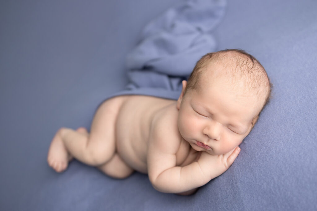 Clifton, NJ newborn photographer captures a sleepy baby peacefully posed on a soft blue blanket during a studio session.