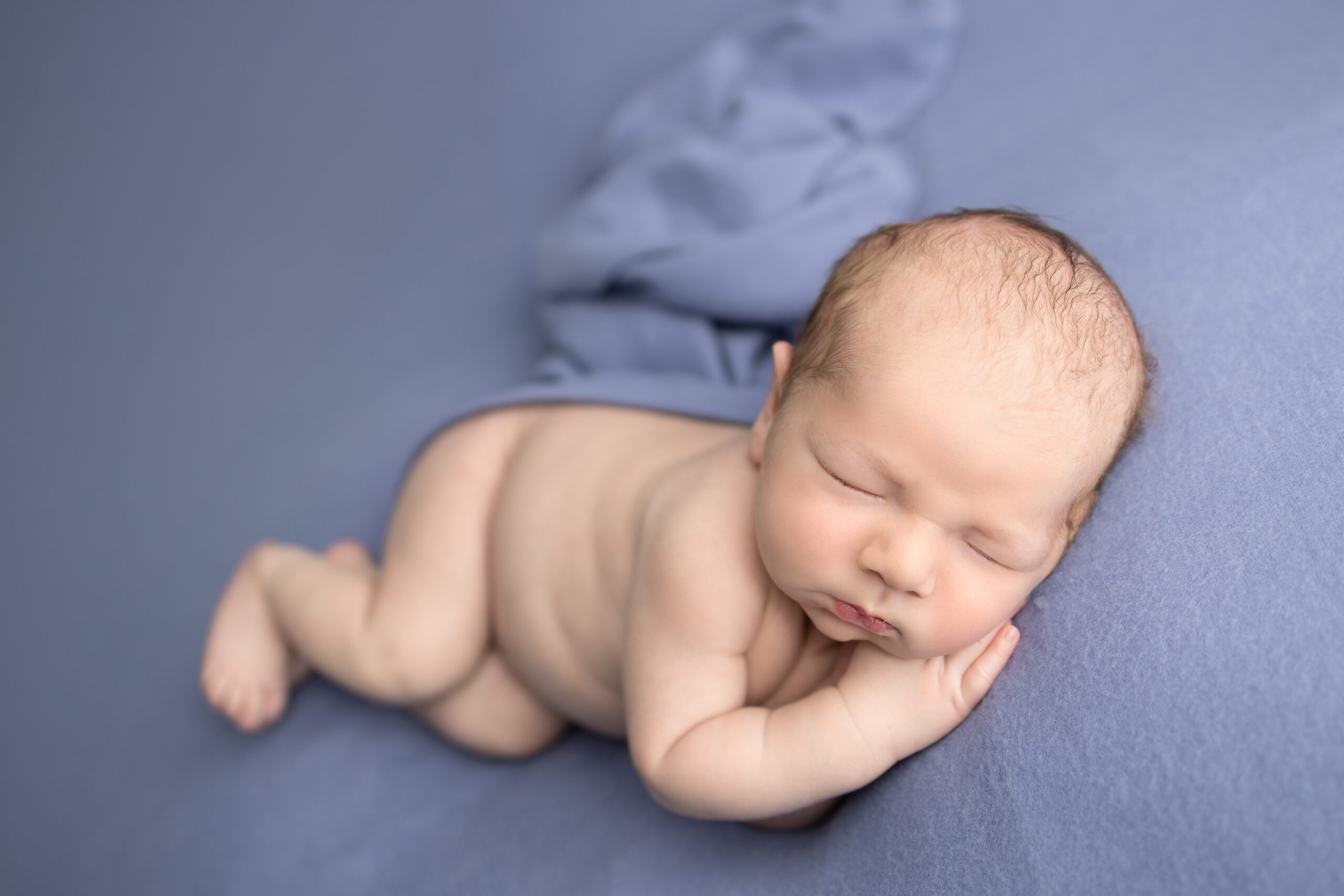 Clifton, NJ newborn photographer captures a sleepy baby peacefully posed on a soft blue blanket during a studio session.