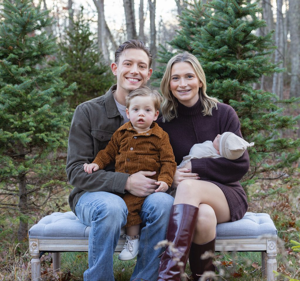 Parents cuddle their baby among evergreen trees during a warm and joyful holiday family photo session.