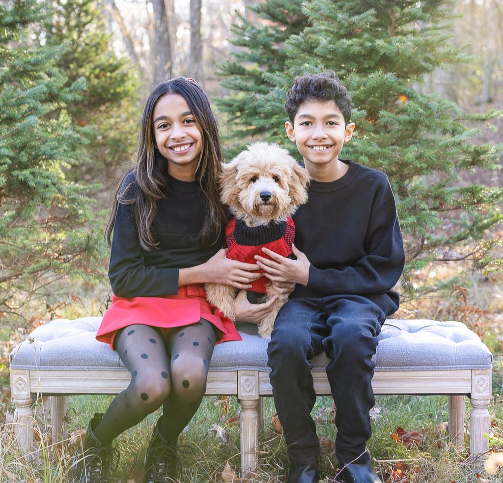 Two siblings smile with their dog during a cozy Christmas tree farm family photo session.
