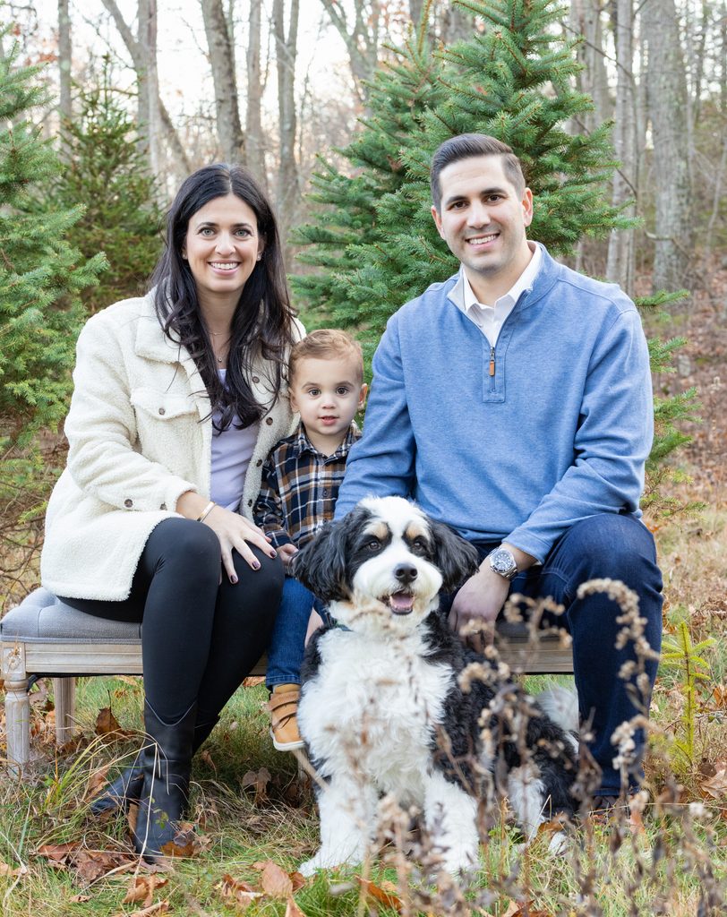 Parents and child pose with their dog among Christmas trees during a festive family photo session.